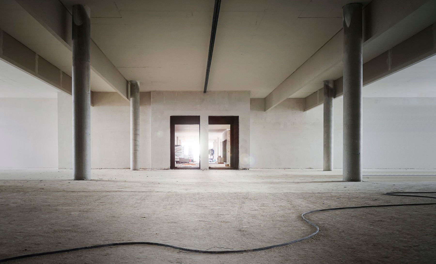 Entry hall as a bare shell: grey concrete floor, unplastered walls, an open doorway at the far end.