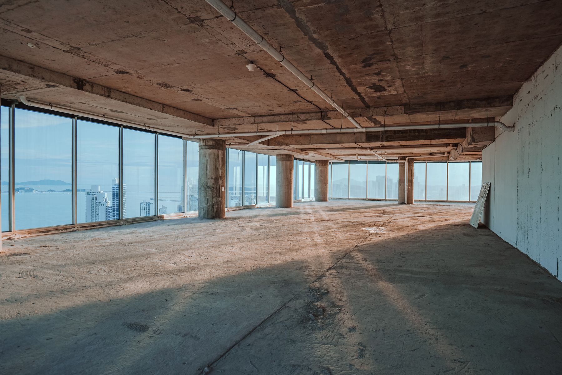 Living room as a bare shell: raw slab floor and a stripped window wall looking out over the city.