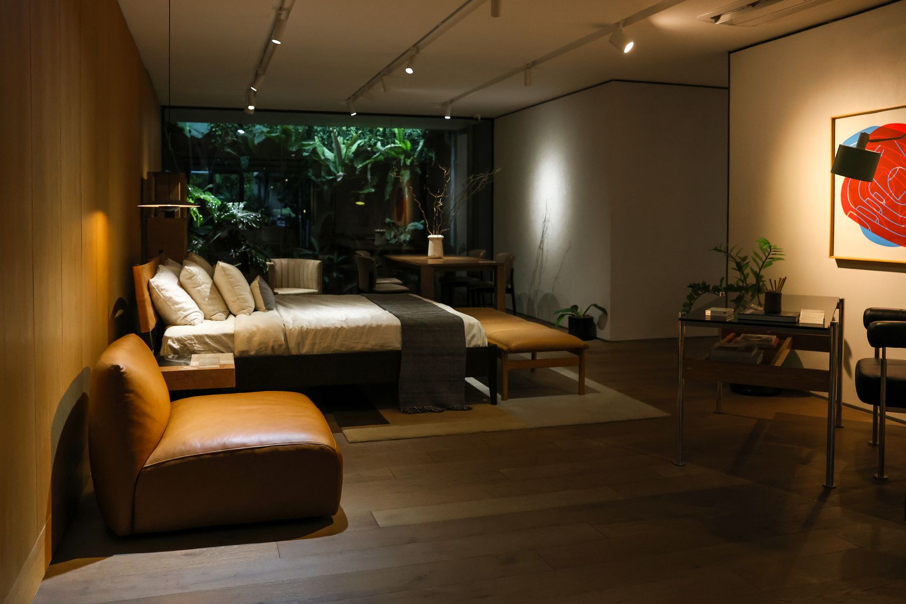 The finished living room at dusk: low seating, linen upholstery, a writing desk and planting against full-height glazing.
